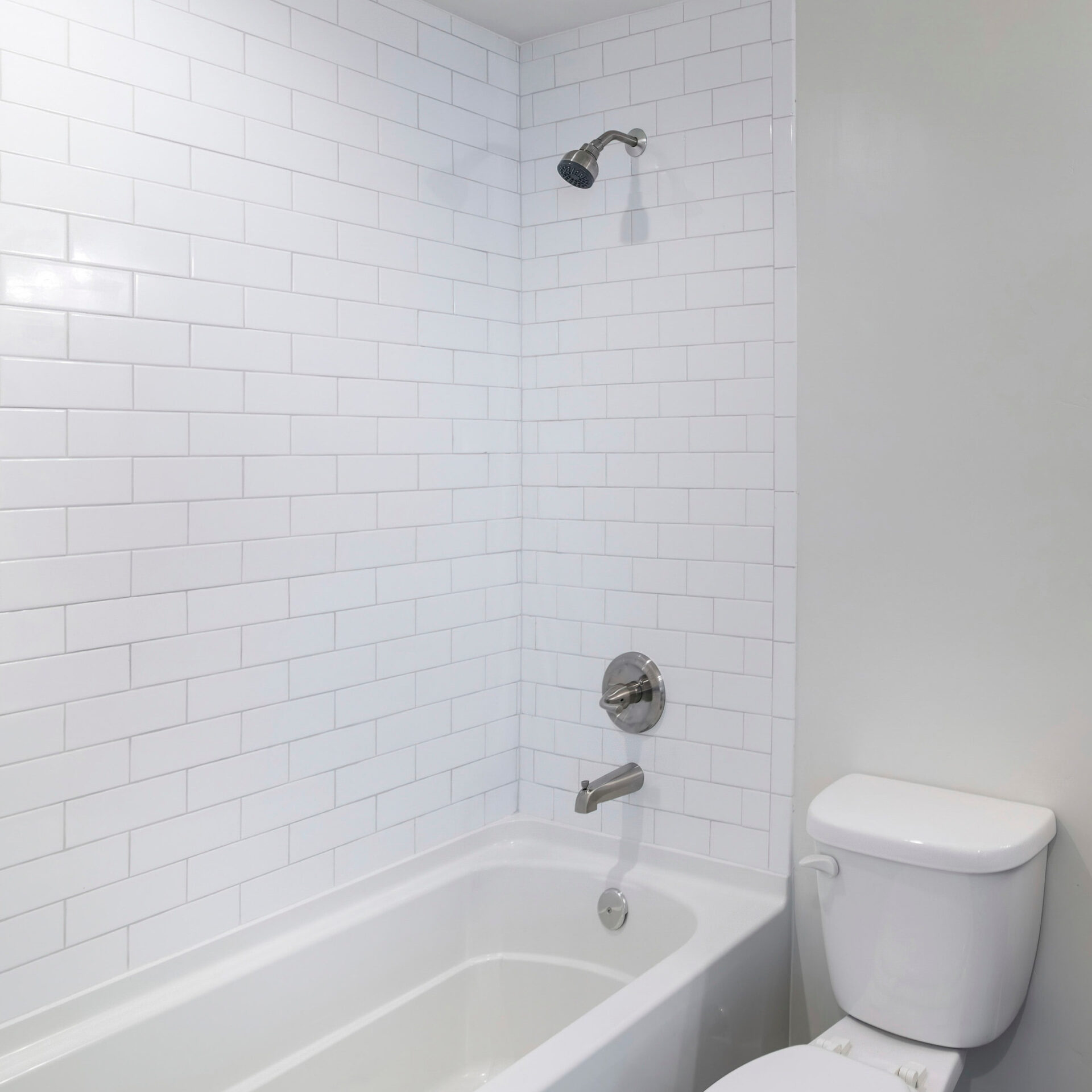 Midrange bathroom remodel with white tub and toilet and subway tile surround